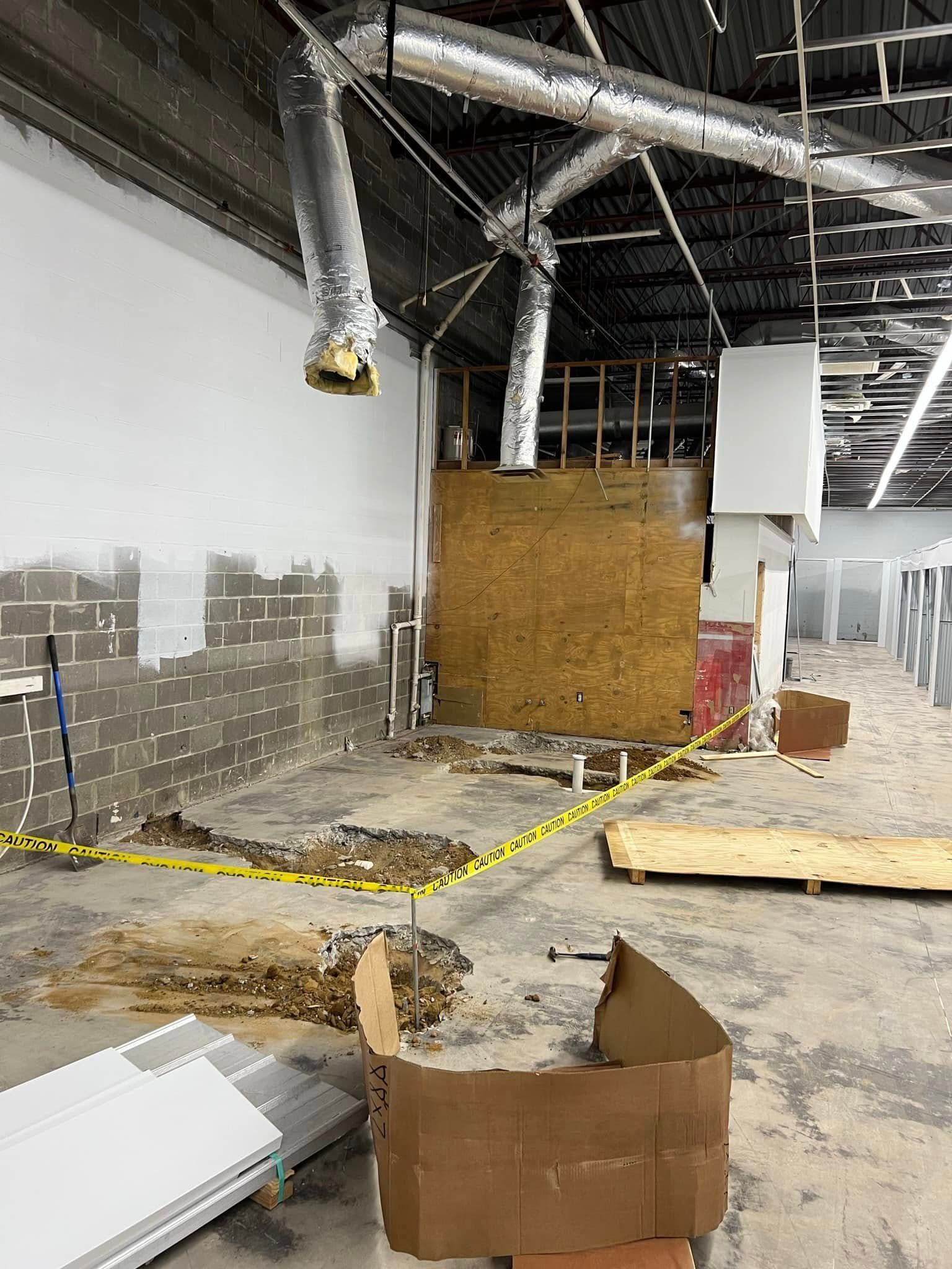 Construction site interior with debris, plywood barriers, and exposed ductwork near a concrete wall