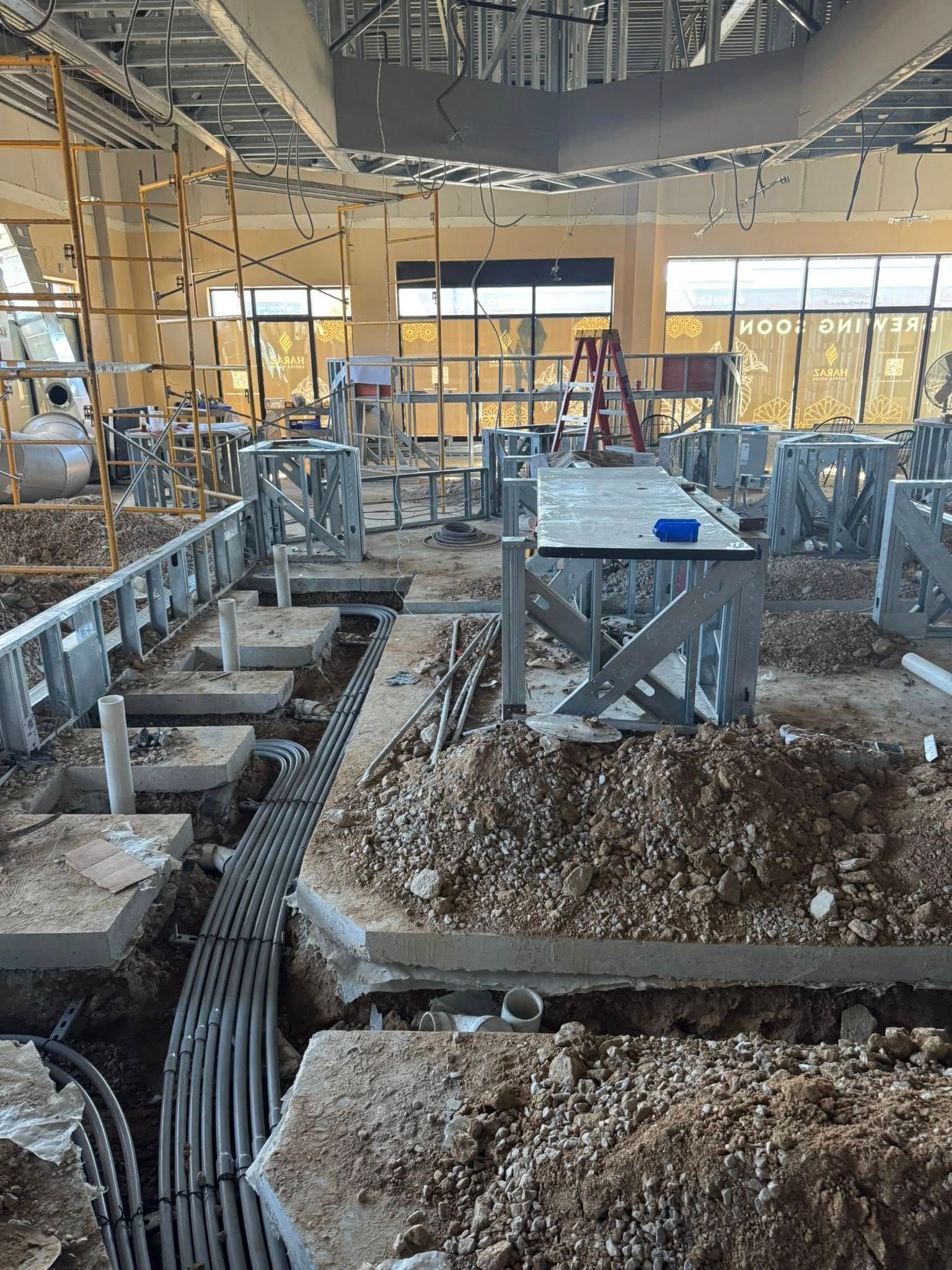 Construction site interior with rebar, gravel piles, and scaffolding under a partially built concrete floor