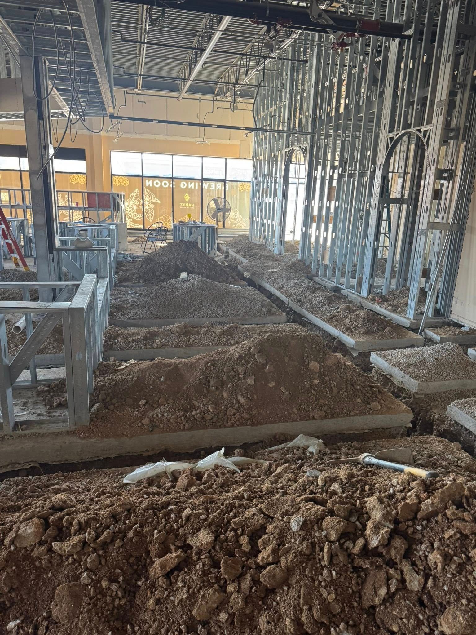Indoor construction site with dirt trenches, exposed framing, and scattered building materials