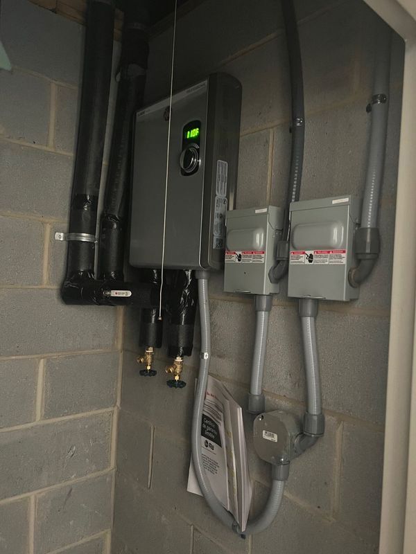 Utility meters and control boxes mounted on a gray brick wall with pipes and cables.