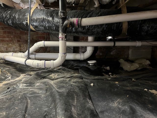 Crawlspace with white PVC pipes and black insulated ductwork over plastic sheeting