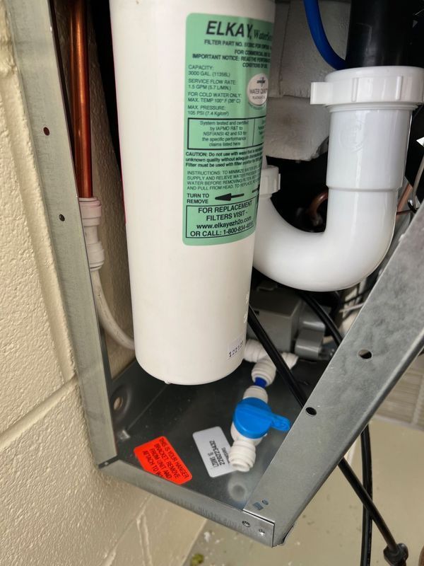 Under-sink water filter system with white and green canisters, white PVC pipe, and blue shutoff valve