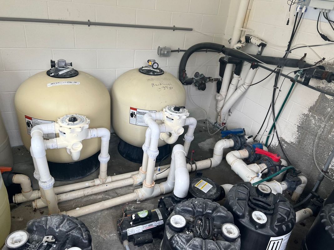 Two beige industrial tanks with white piping and pumps in a utility room.