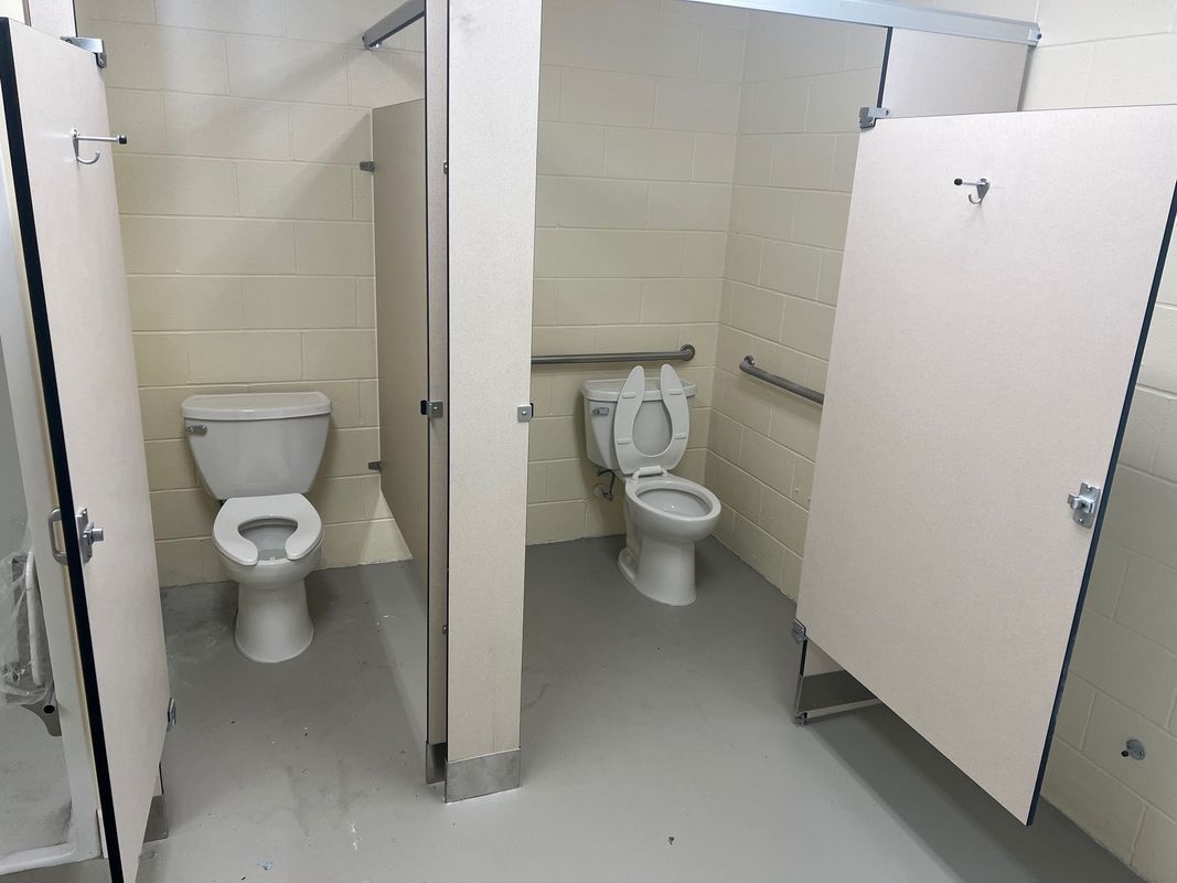 Three restroom stalls with toilets in a beige-tiled public bathroom