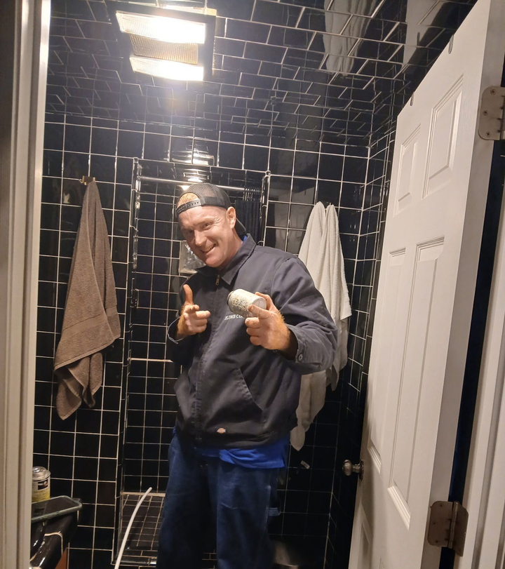 Person smiling and pointing in a tiled bathroom with towels hanging on the wall.