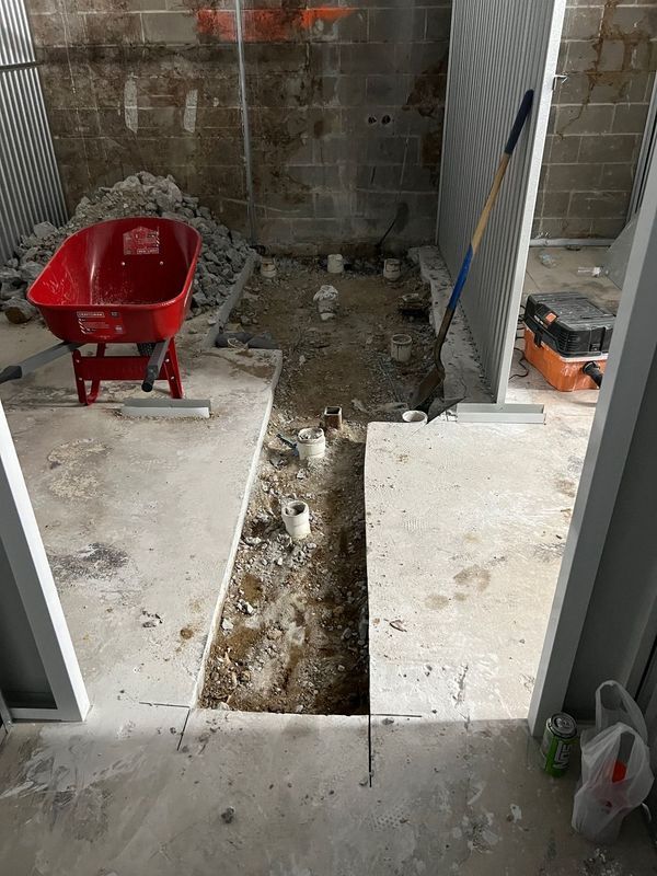 Partially dug-up patio with a red wheelbarrow and concrete slabs beside a brick wall