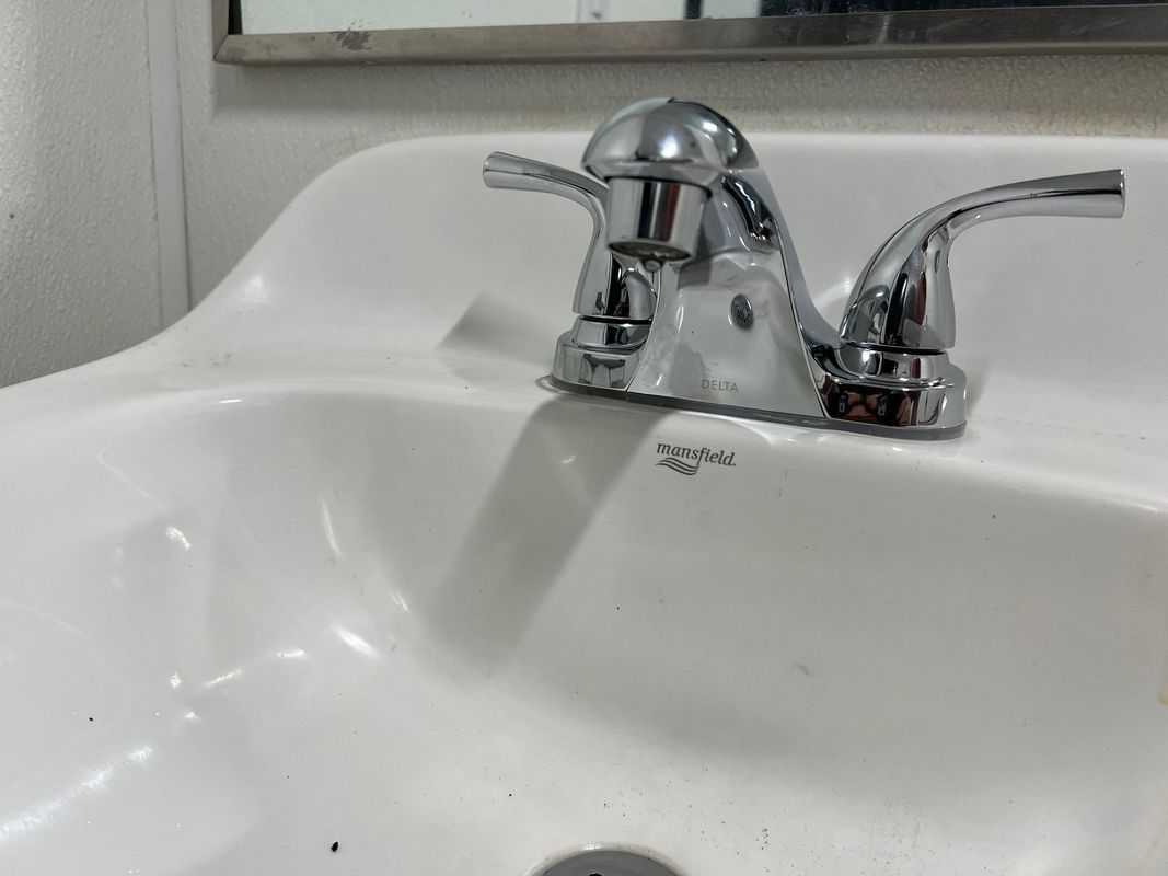White bathroom sink with chrome faucet and handles against a tiled wall.