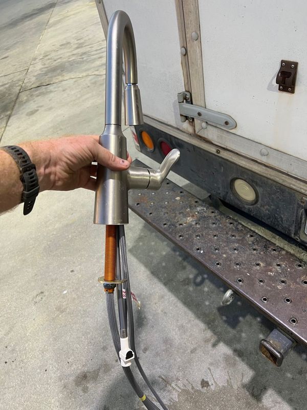 Hand holding a silver metal tool with orange spring detail beside a truck trailer ramp