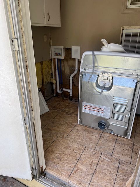 Utility room with a large metal appliance on tiled floor, near exposed pipes and wall fixtures.