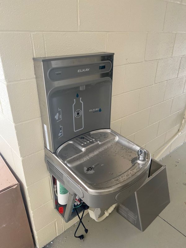 Stainless steel wall-mounted drinking fountain with bottle filler in a tiled hallway