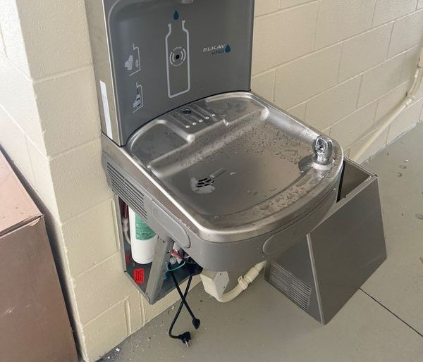 Stainless steel drinking fountain mounted on a tiled wall with an open side panel.
