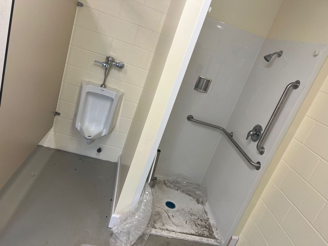 Bathroom with urinal on left and accessible shower stall on right, both with grab bars.