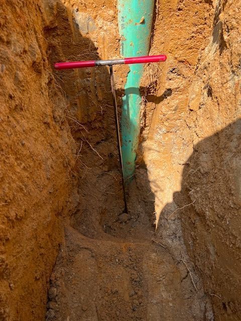 Excavation trench with a turquoise pipe and a red marker rod against orange dirt walls