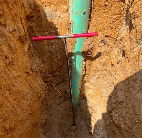 Trench with a green pipe and a red rod crossing it in exposed soil