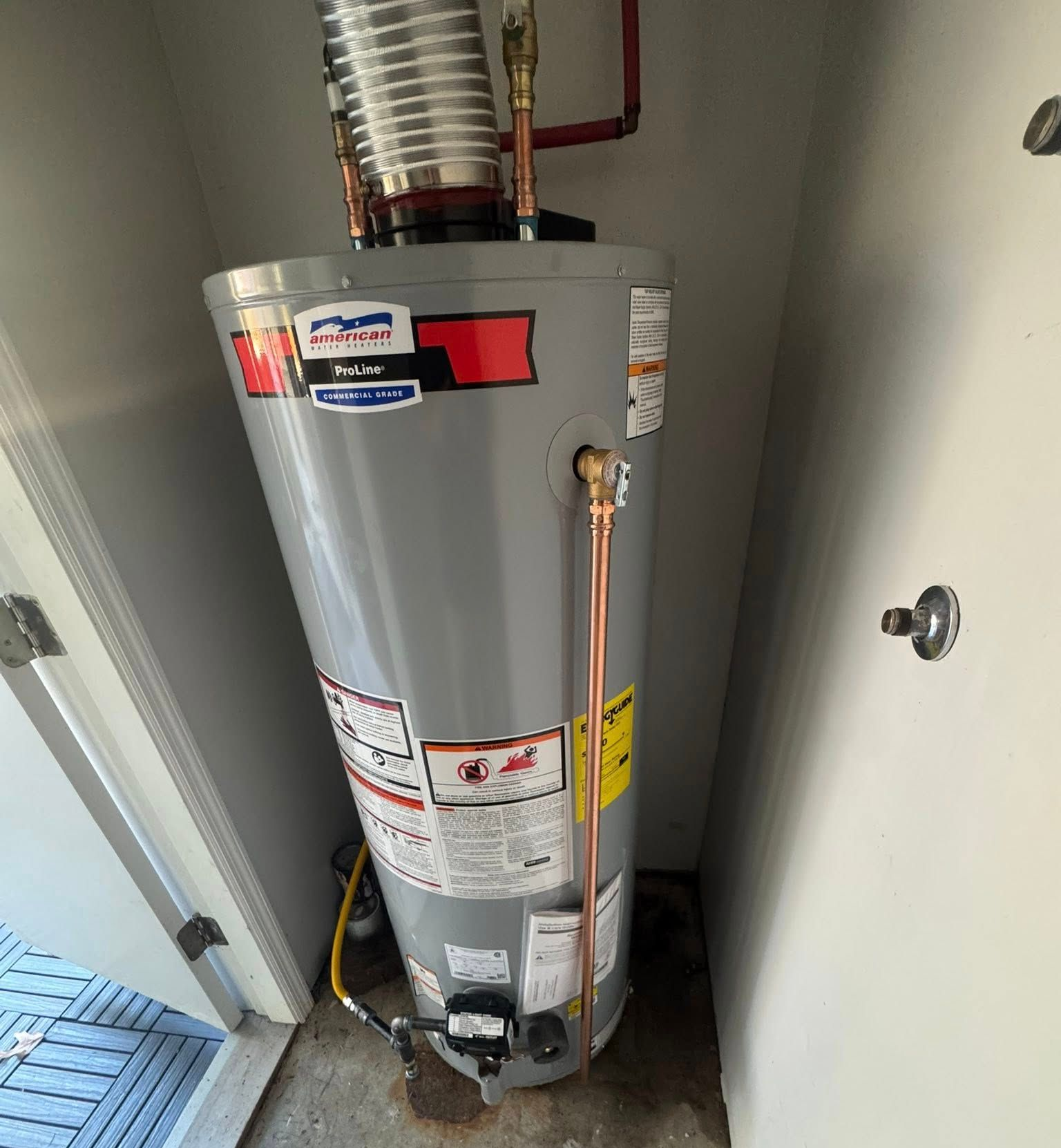 Gray water heater in a narrow utility closet with visible pipes and venting.