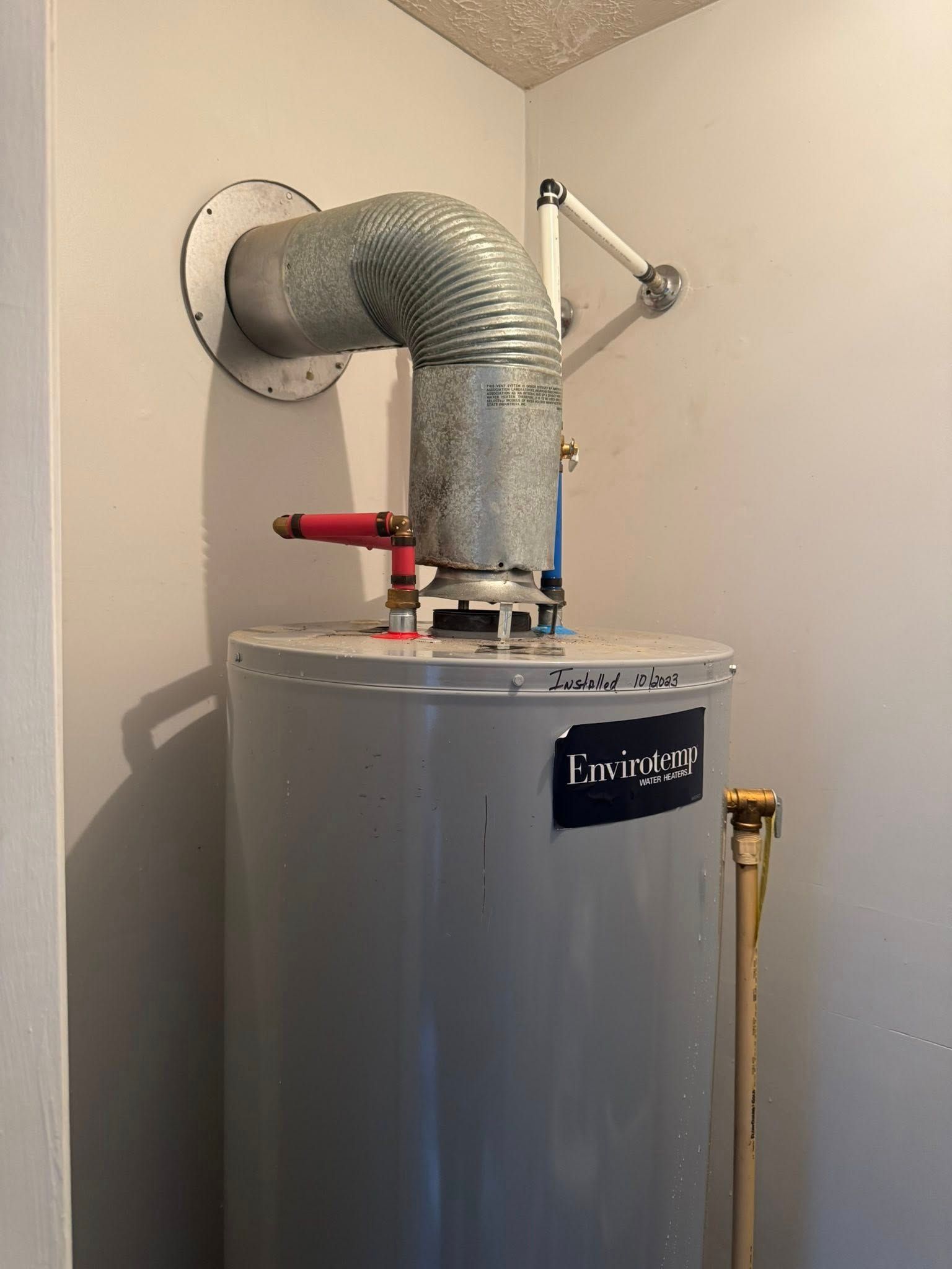 Water heater in a utility closet with silver vent piping and a red valve handle.