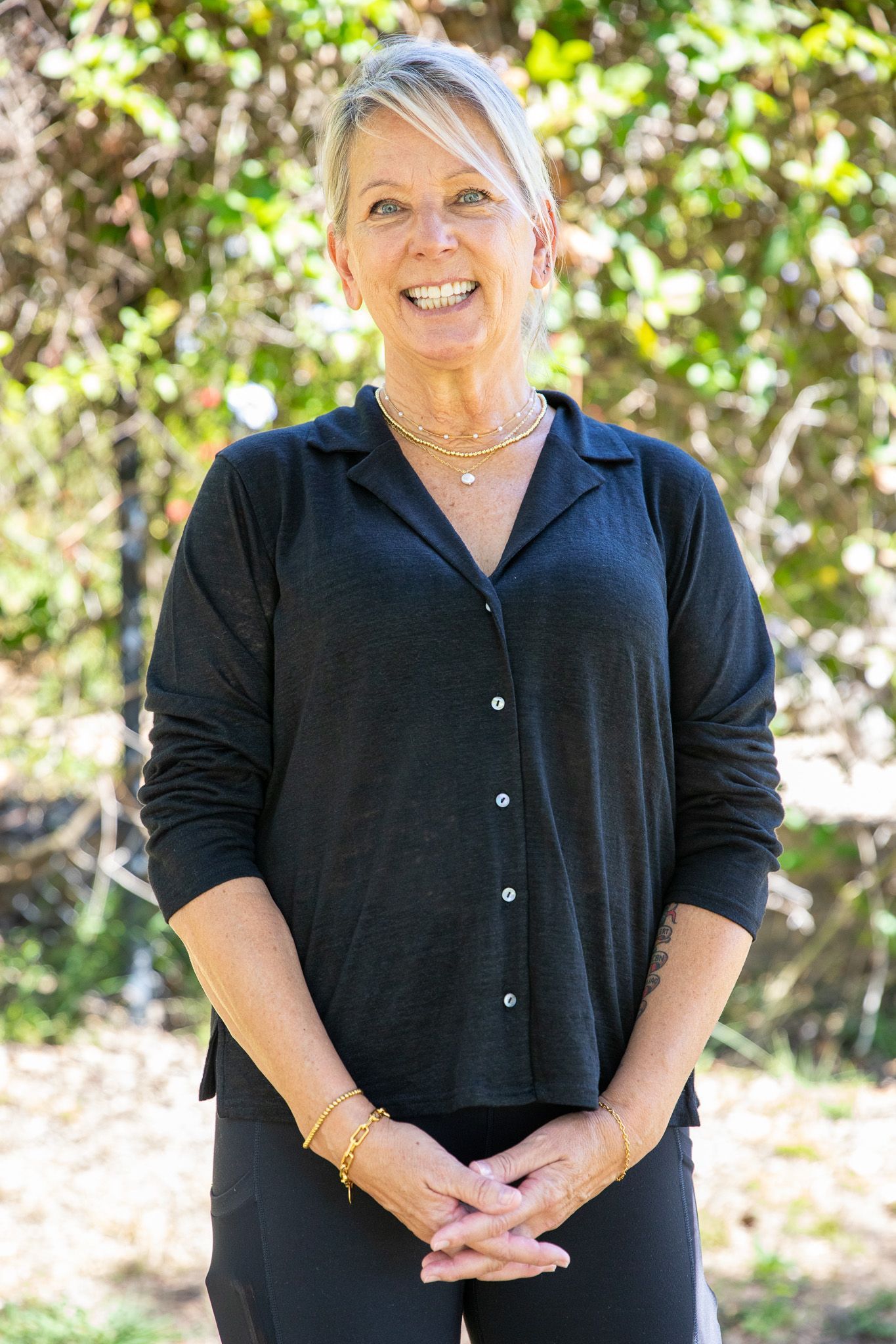 Woman with blonde hair smiles in black shirt outdoors.