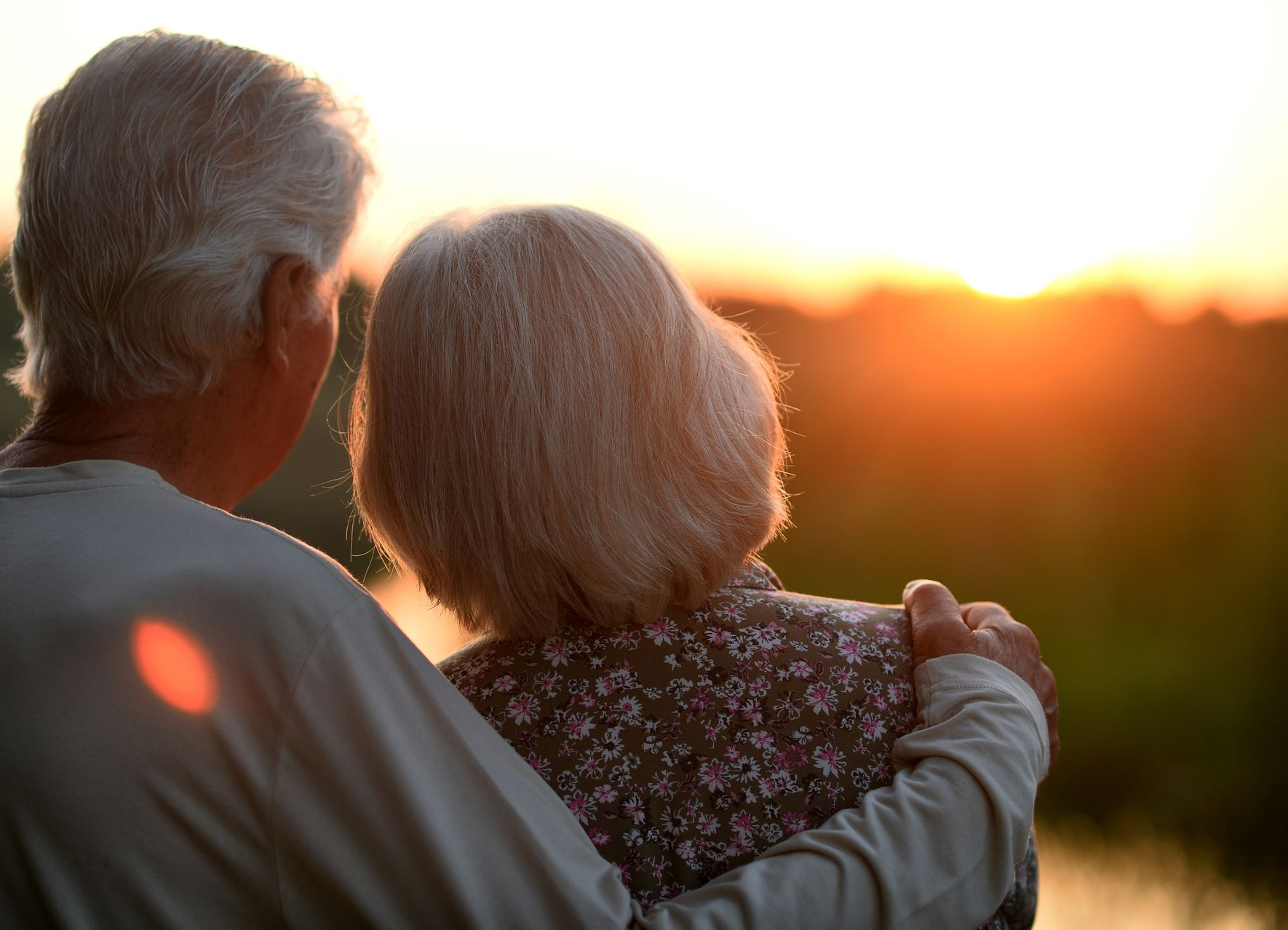Two people sit close together at sunset, facing a glowing horizon.