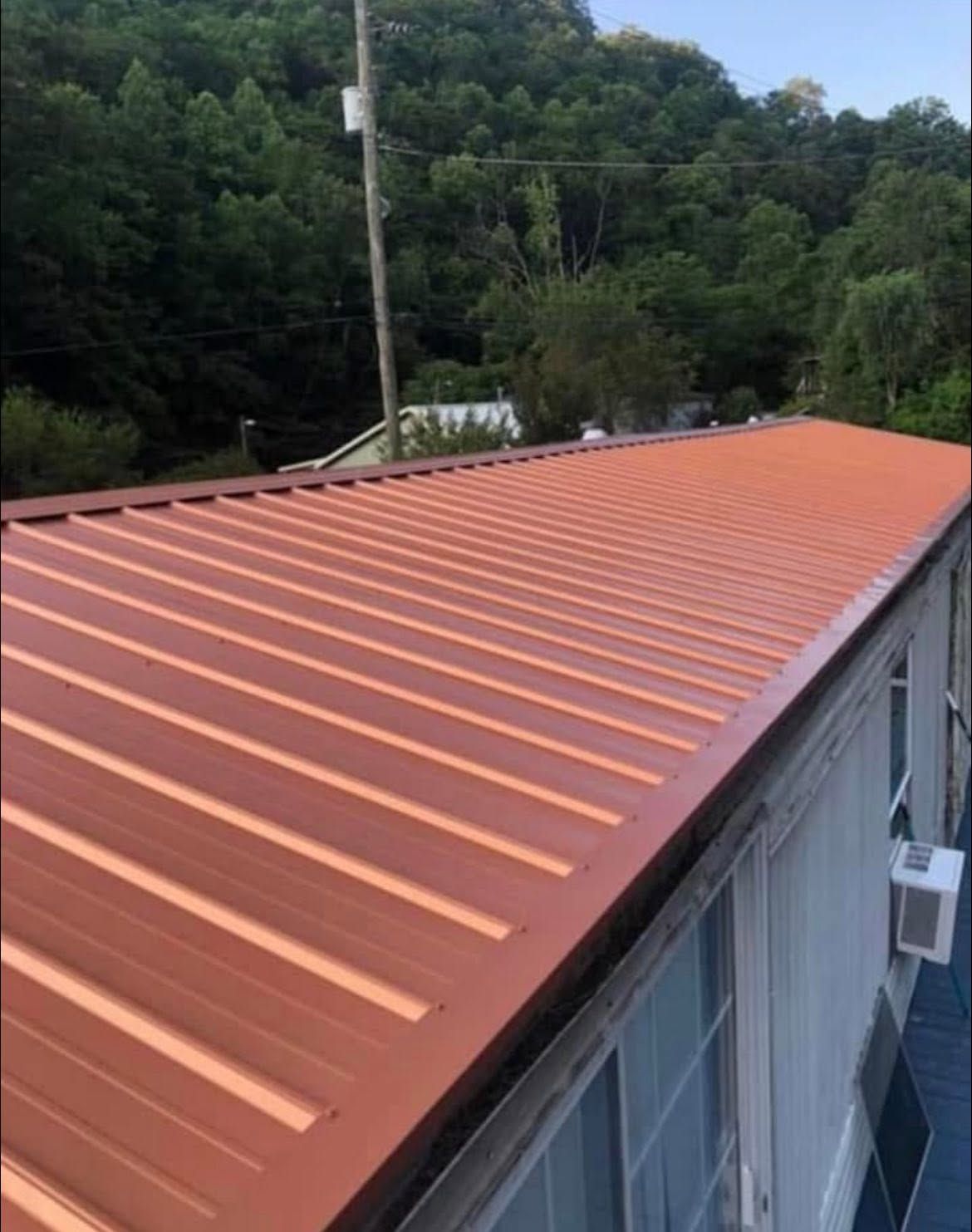 Orange metal roof on a building, viewed from above with green trees in the background