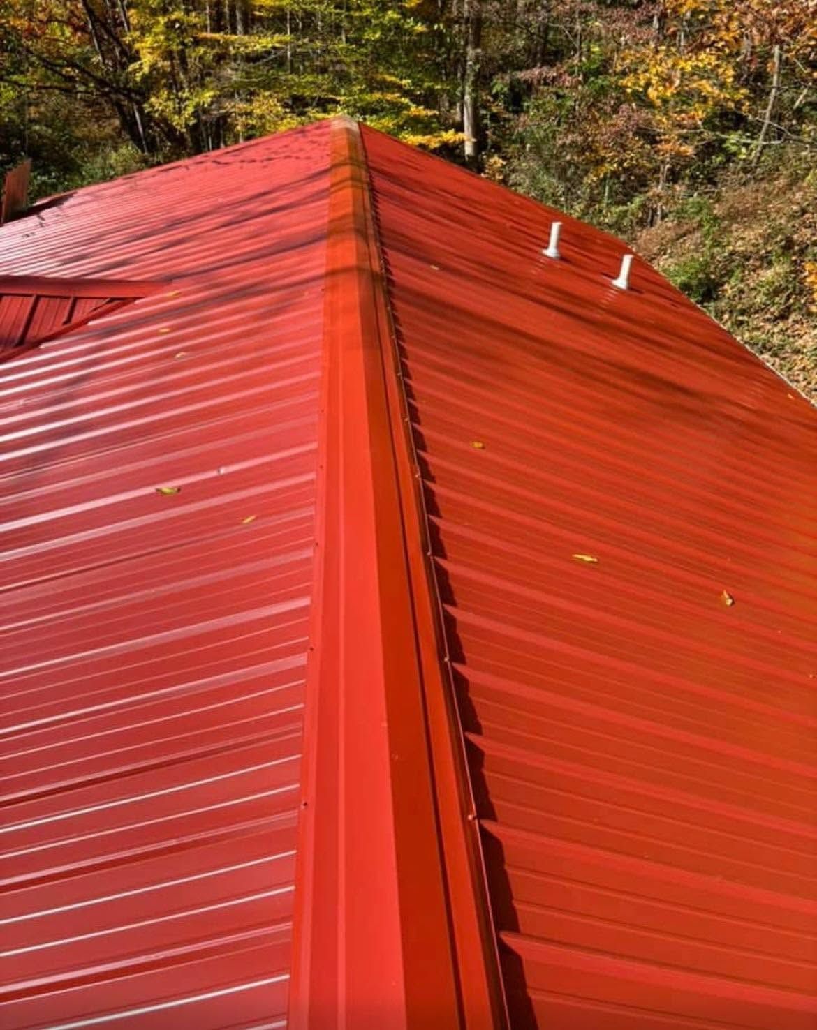 Red metal roof of a building against autumn trees