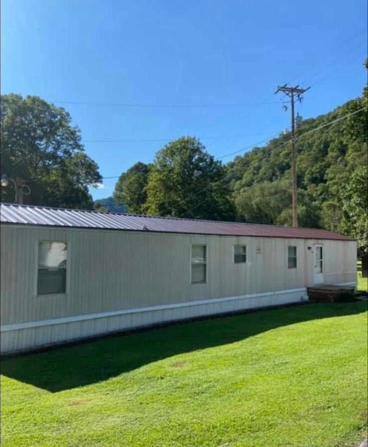 White mobile home on a green lawn with trees and hills under a clear blue sky