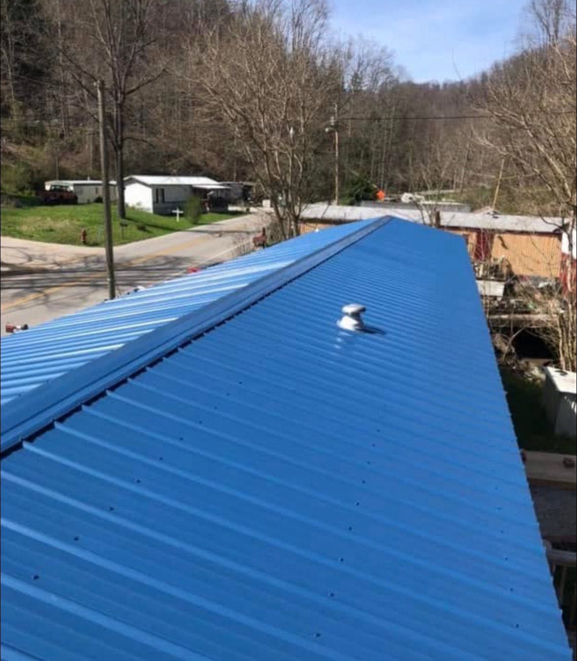 Blue metal roof on a building, viewed from above with trees and houses in the background.