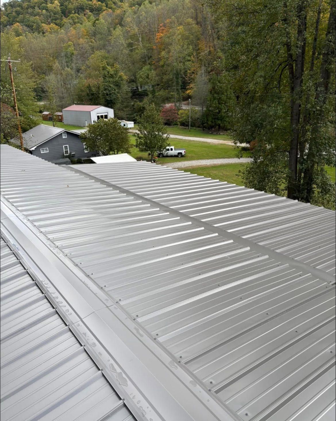 Metal roof overlooking a wooded rural property with houses and a driveway