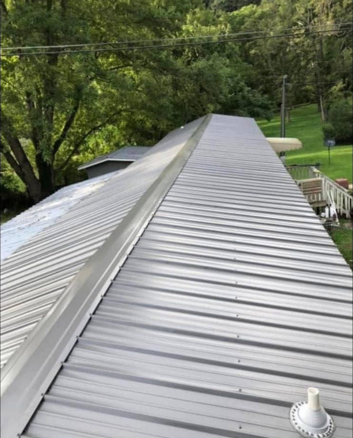 Long gray metal roof with roof ridge, surrounded by green trees and a yard.