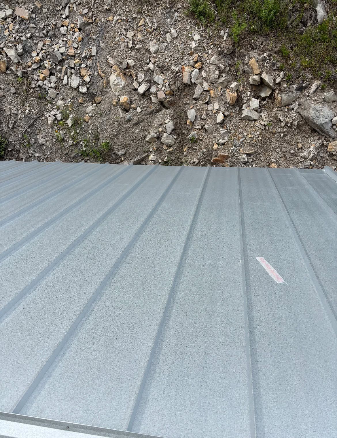 Gray corrugated metal roof below a rocky dirt slope with sparse grass