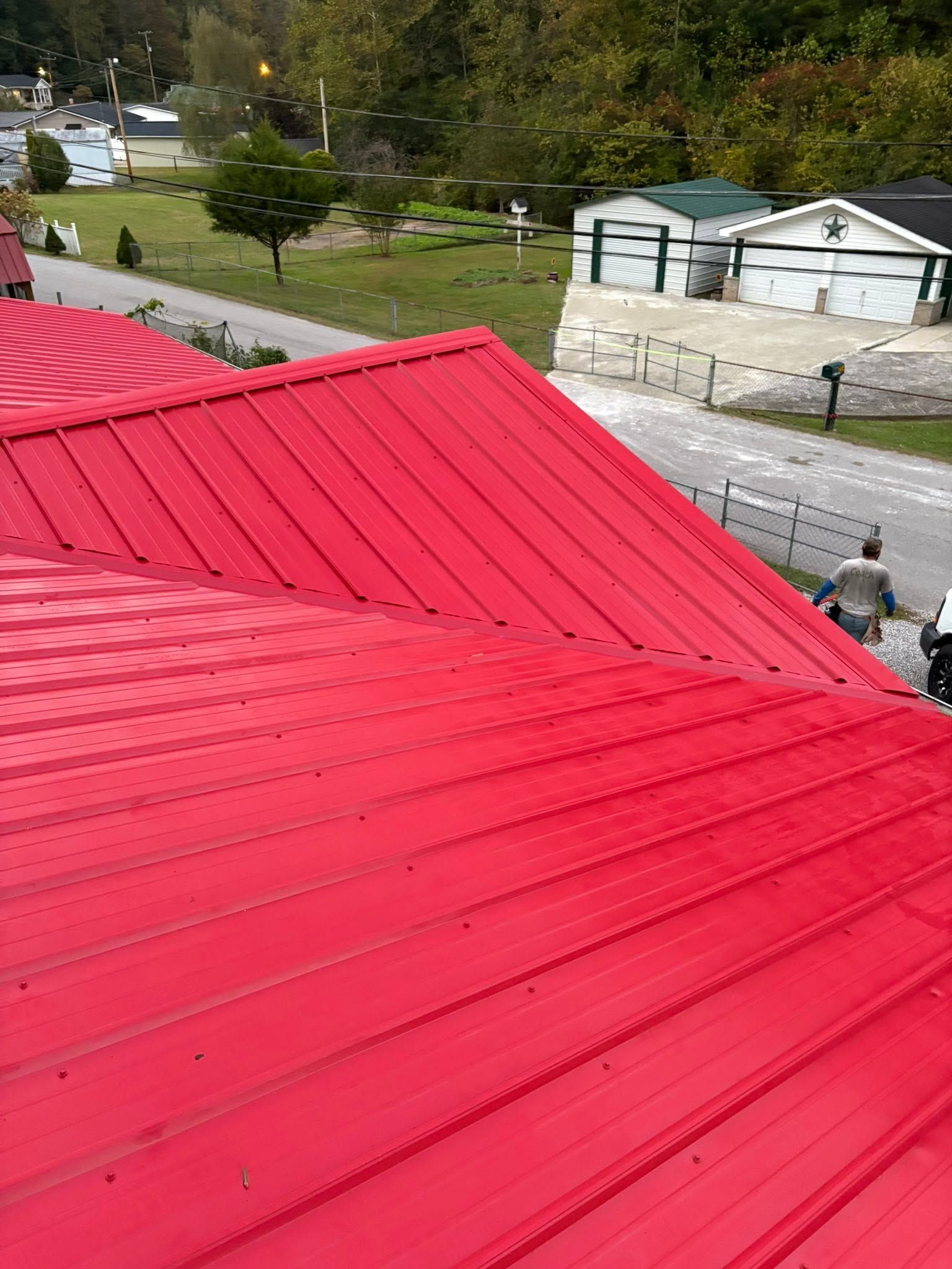 Bright red metal roof overlooking a paved courtyard, trees, and a small white building