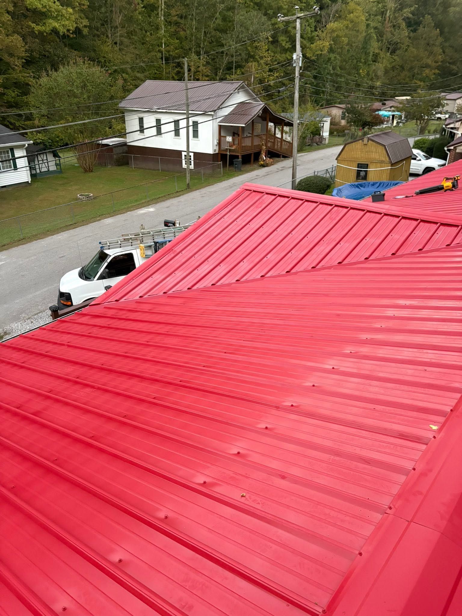 Red metal roof in foreground with a rural road, parked cars, and houses in the background