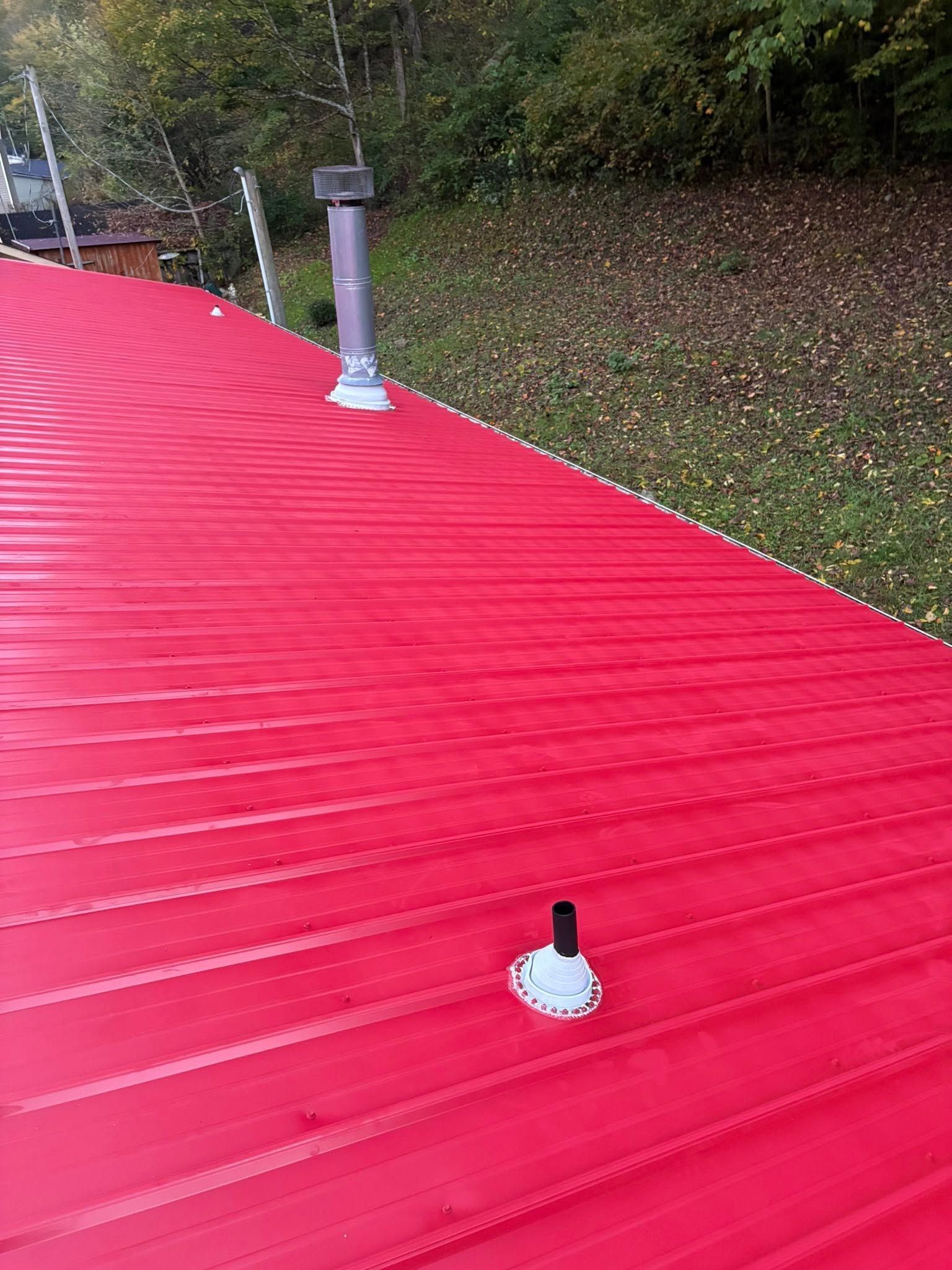 Bright red corrugated roof with two vent pipes beside a wooded hillside