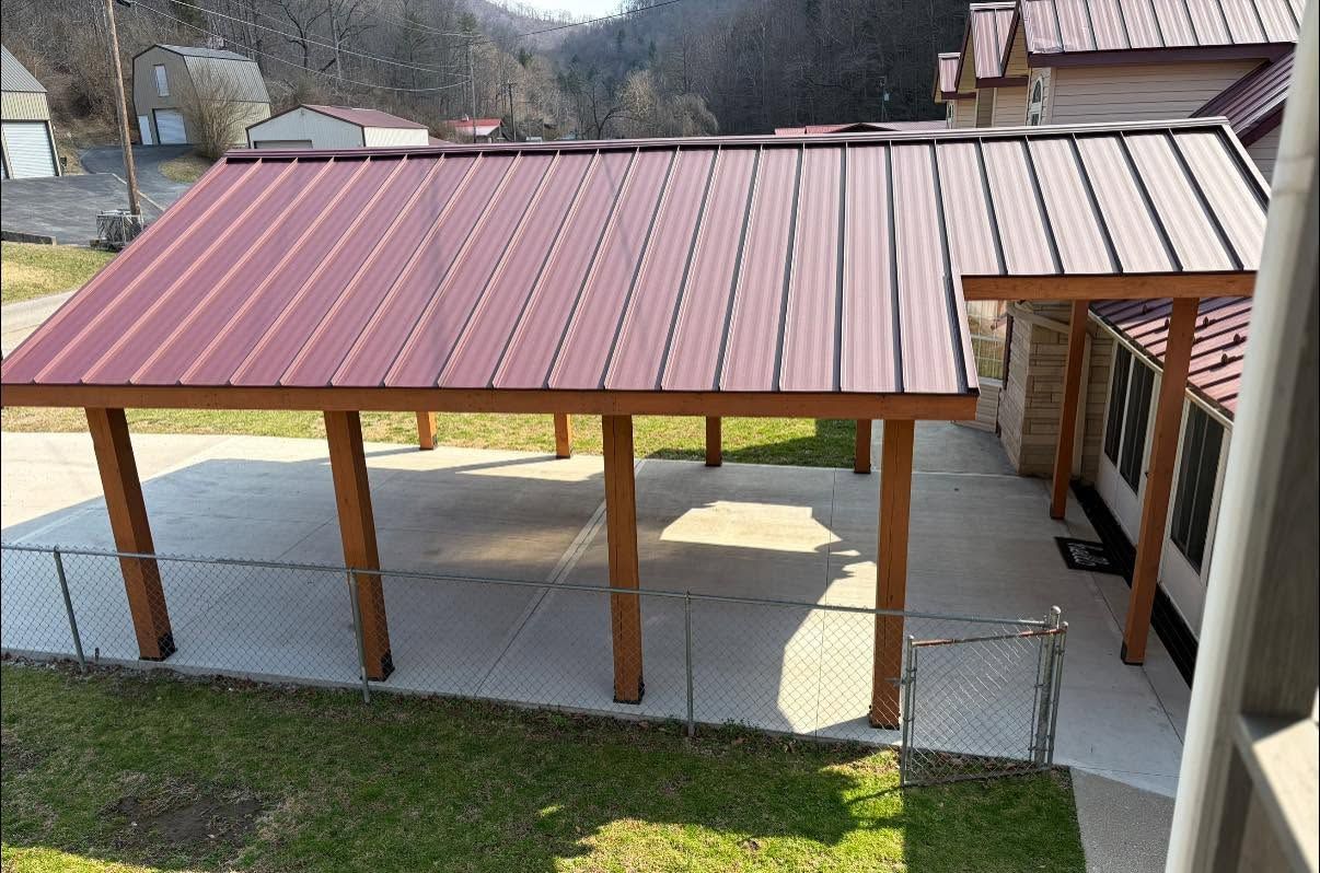 Covered driveway or carport with a red metal roof supported by wooden posts next to a house