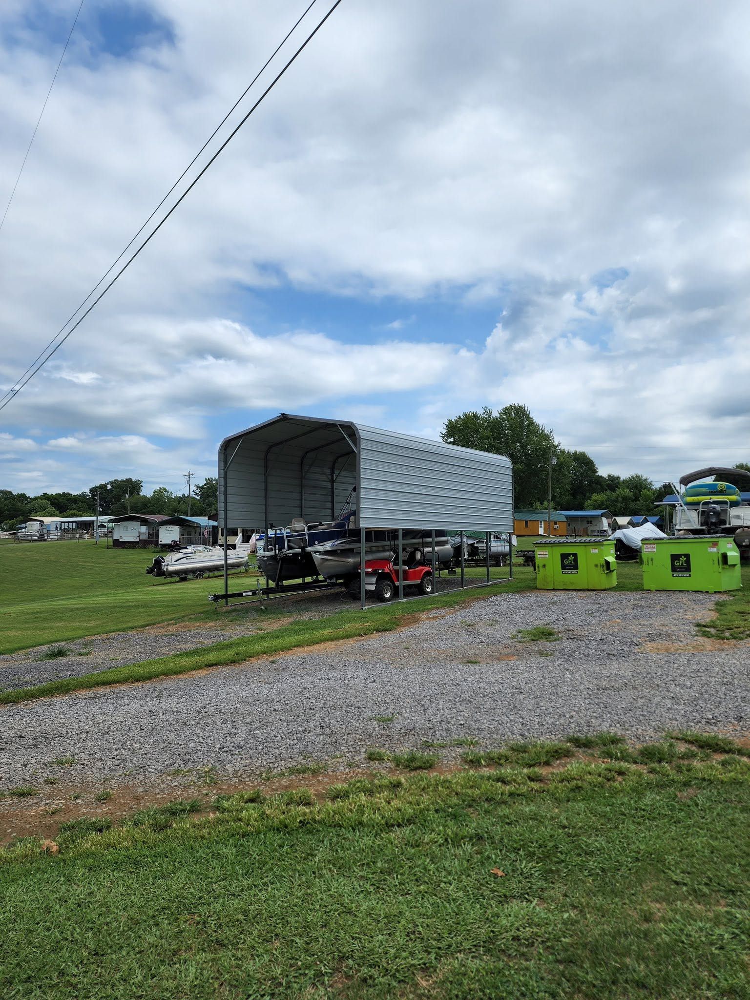 Gray truck trailer parked on a gravel lot beside bright green portable toilets under a cloudy sky
