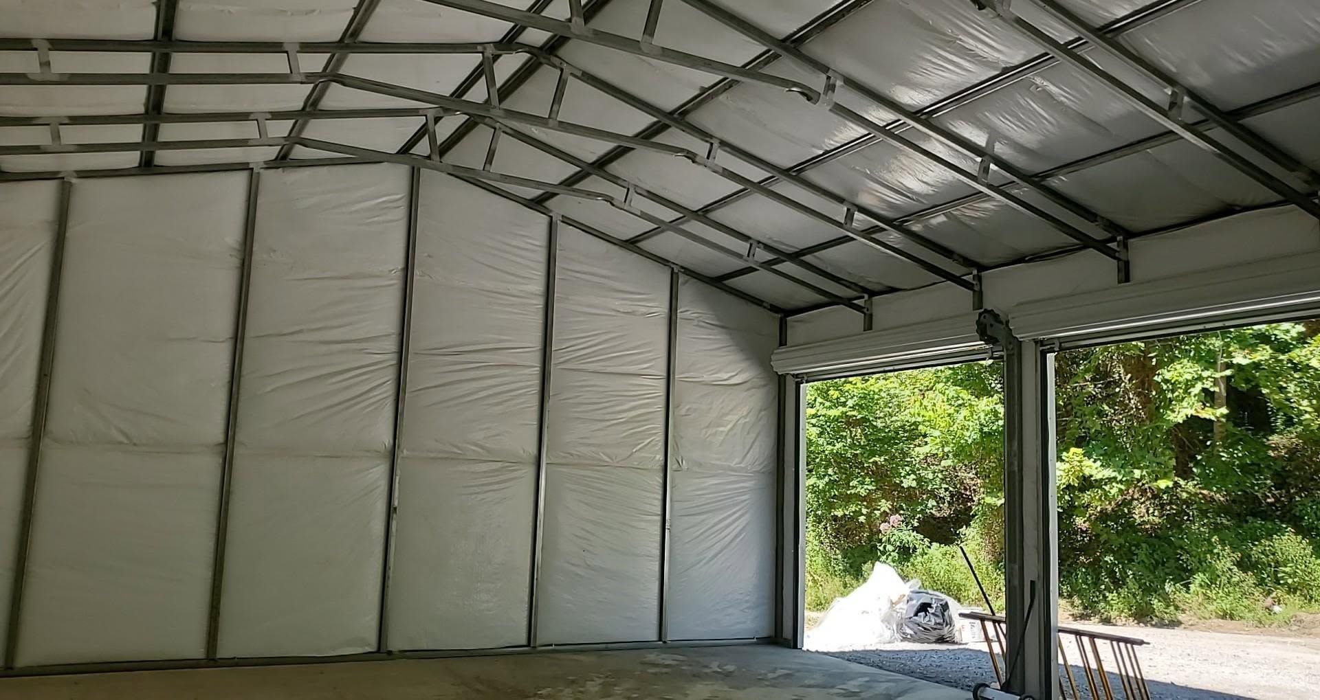 Empty metal-framed warehouse interior with white insulated wall panels and open side showing greenery outside