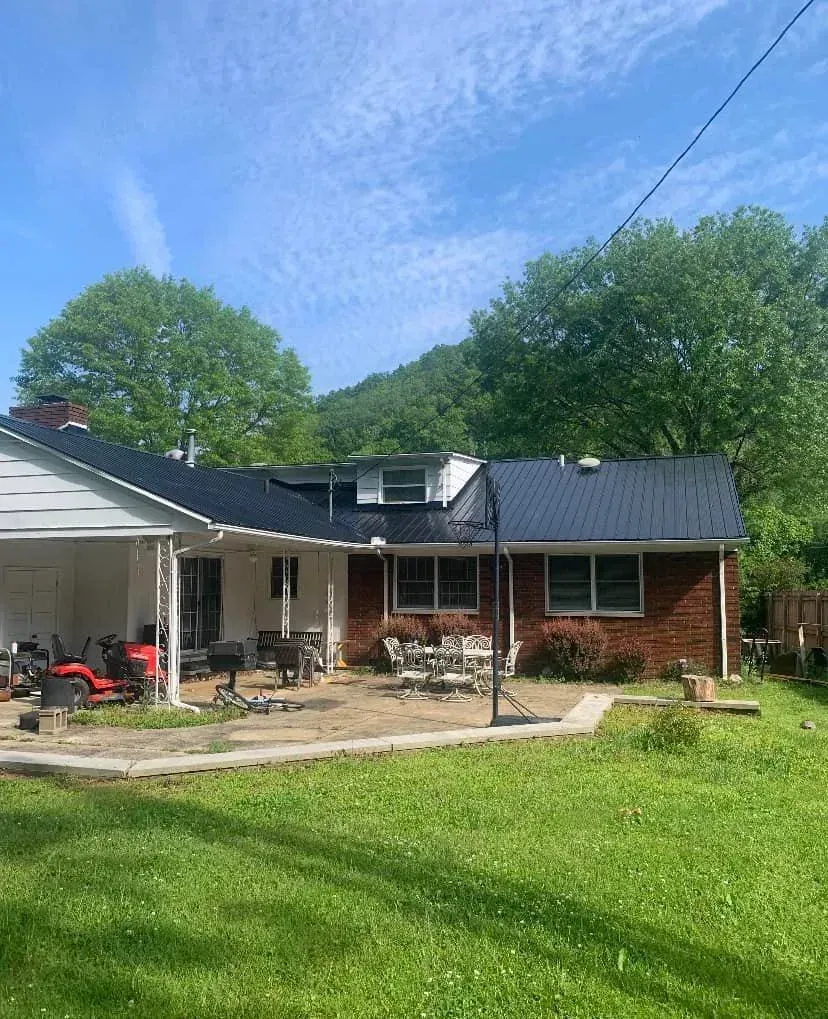 Single-story brick house with a dark roof, patio furniture, and a green lawn under a blue sky