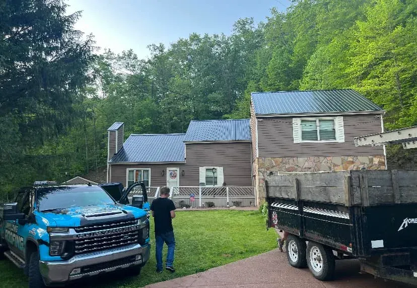 Blue pickup and black trailer in front of a house, with a person standing on the lawn.