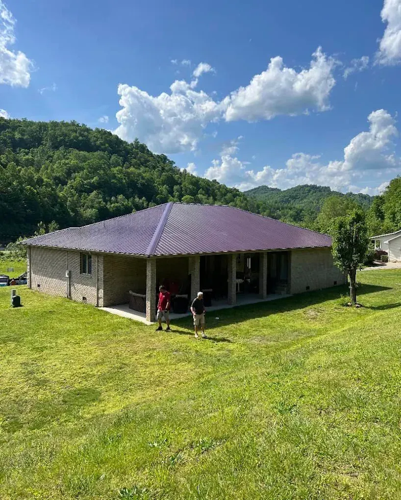 Single-story house with purple roof on a grassy hill, two people standing outside under a bright blue sky.