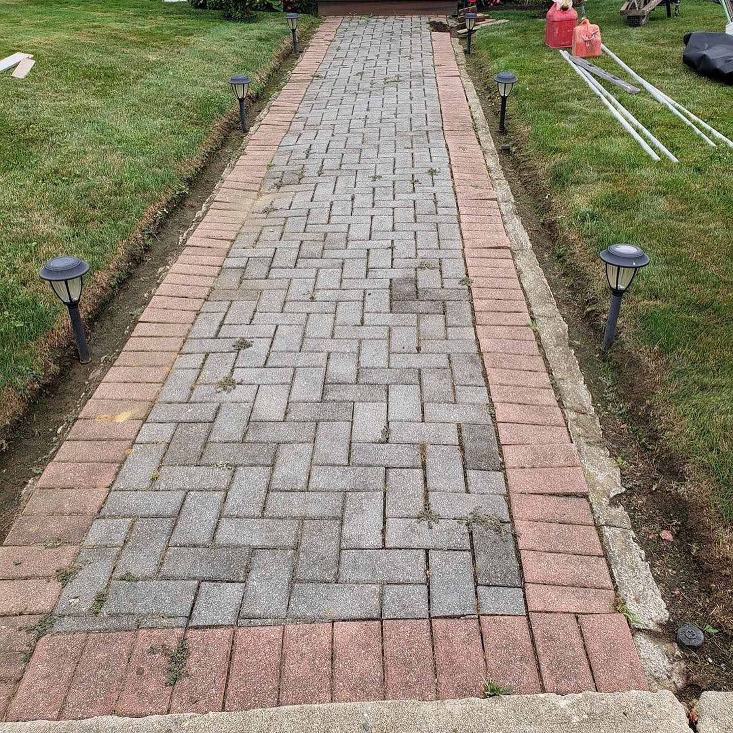 Brick pathway with a red brick border, solar lights, and green grass on either side.