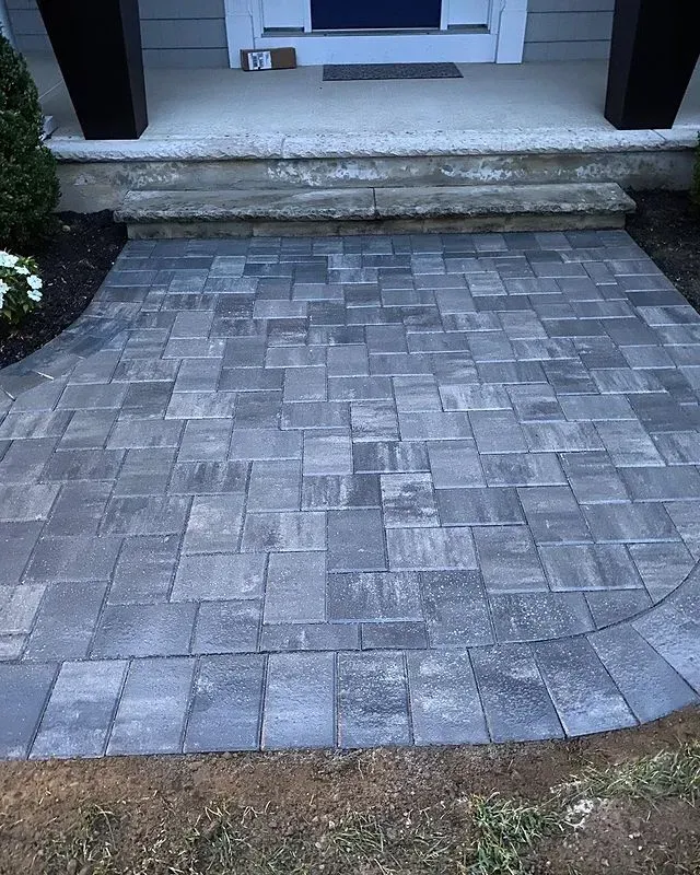Gray brick walkway leading to a house entrance with stone steps.