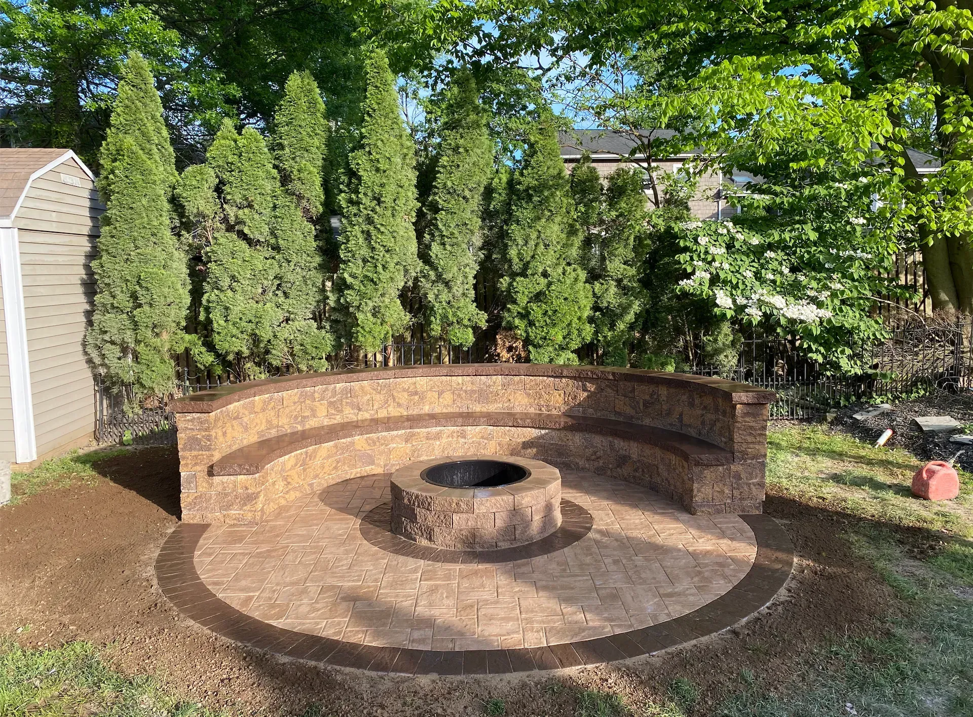 Outdoor fire pit with circular stone seating. Green trees in background.