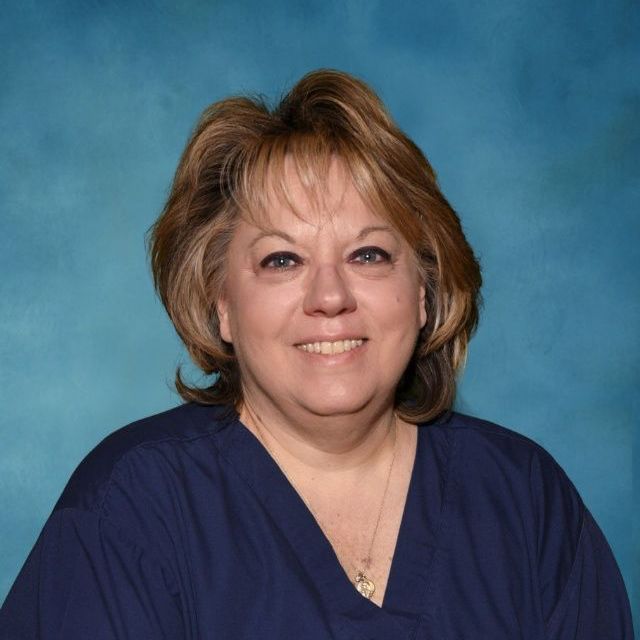 A woman in a blue scrub top is smiling for the camera