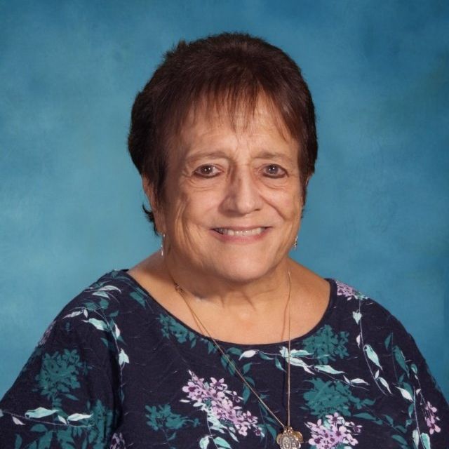 A woman wearing a floral shirt and necklace smiles for the camera