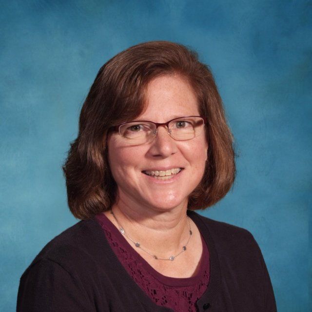 A woman wearing glasses and a necklace smiles for the camera