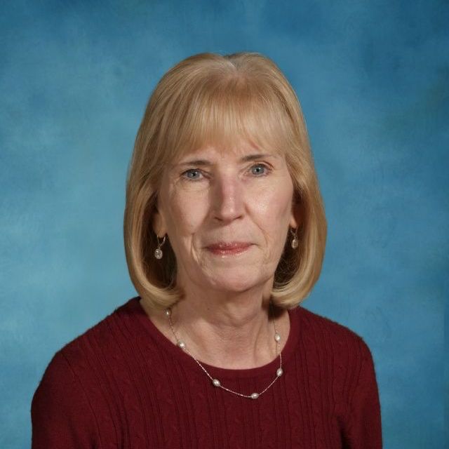 A woman wearing a red sweater and a pearl necklace