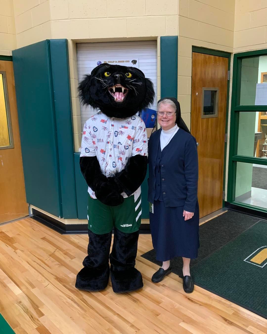 A nun is standing next to a black panther mascot.