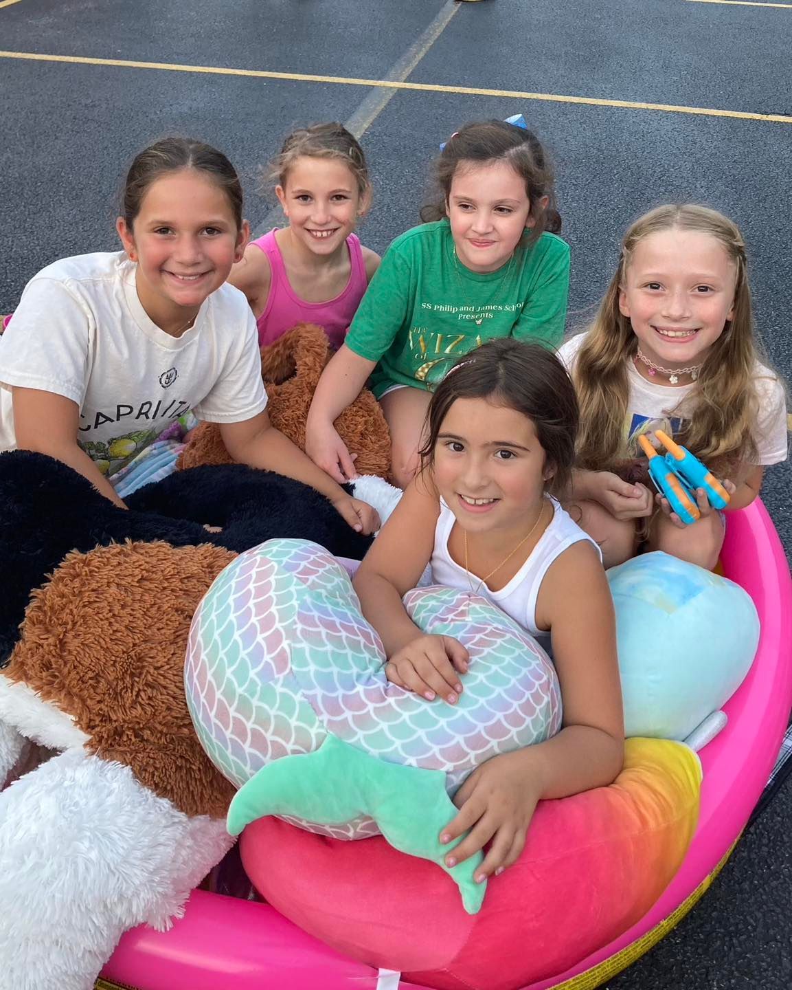 A group of young girls are sitting in a pink boat with stuffed animals.