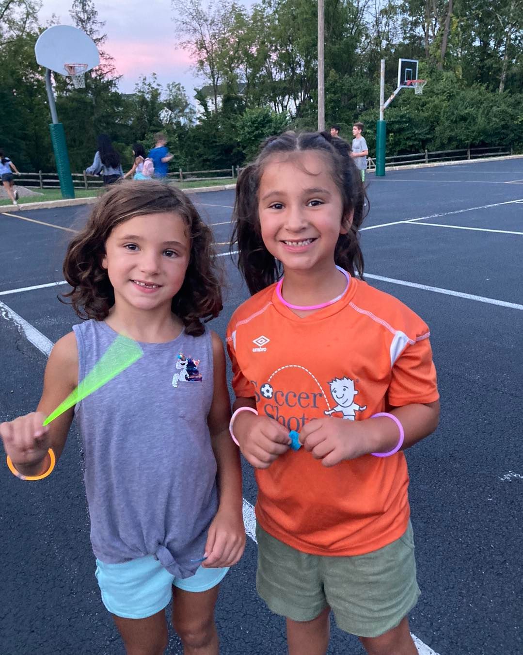 Two young girls are standing next to each other on a basketball court.
