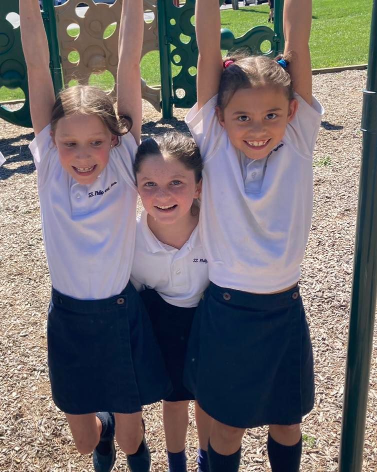 Three girls playing on a playground, hanging from the monkey bars.