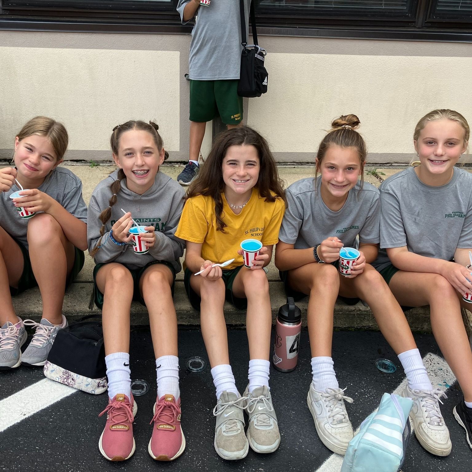A group of young girls are sitting on the sidewalk eating ice cream